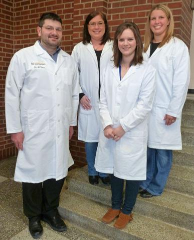 Four people in lab coats standing on steps, smiling