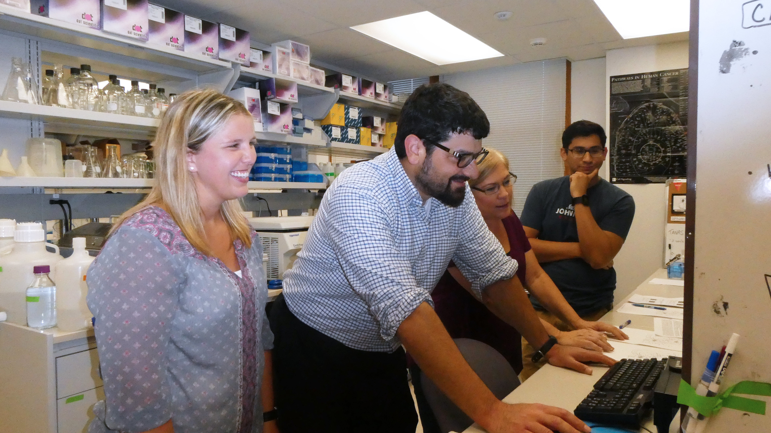 Dr. Tanas and lab members looking at a computer screen and smiling